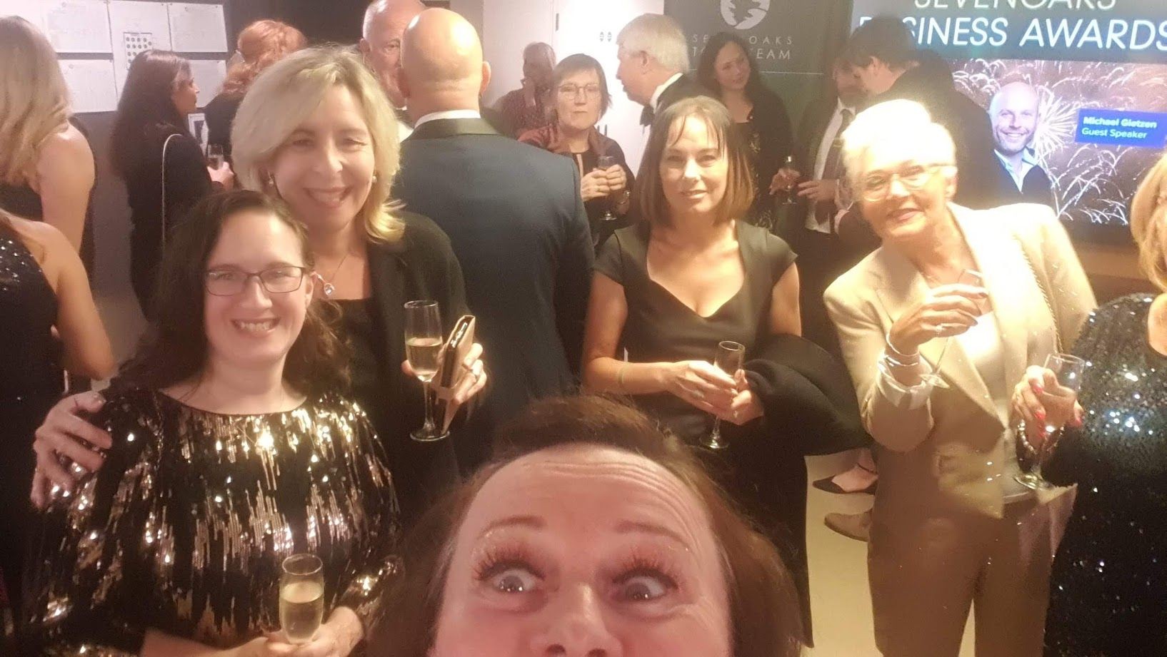 People dressed formally, smiling and holding glasses of champagne at a business awards event.