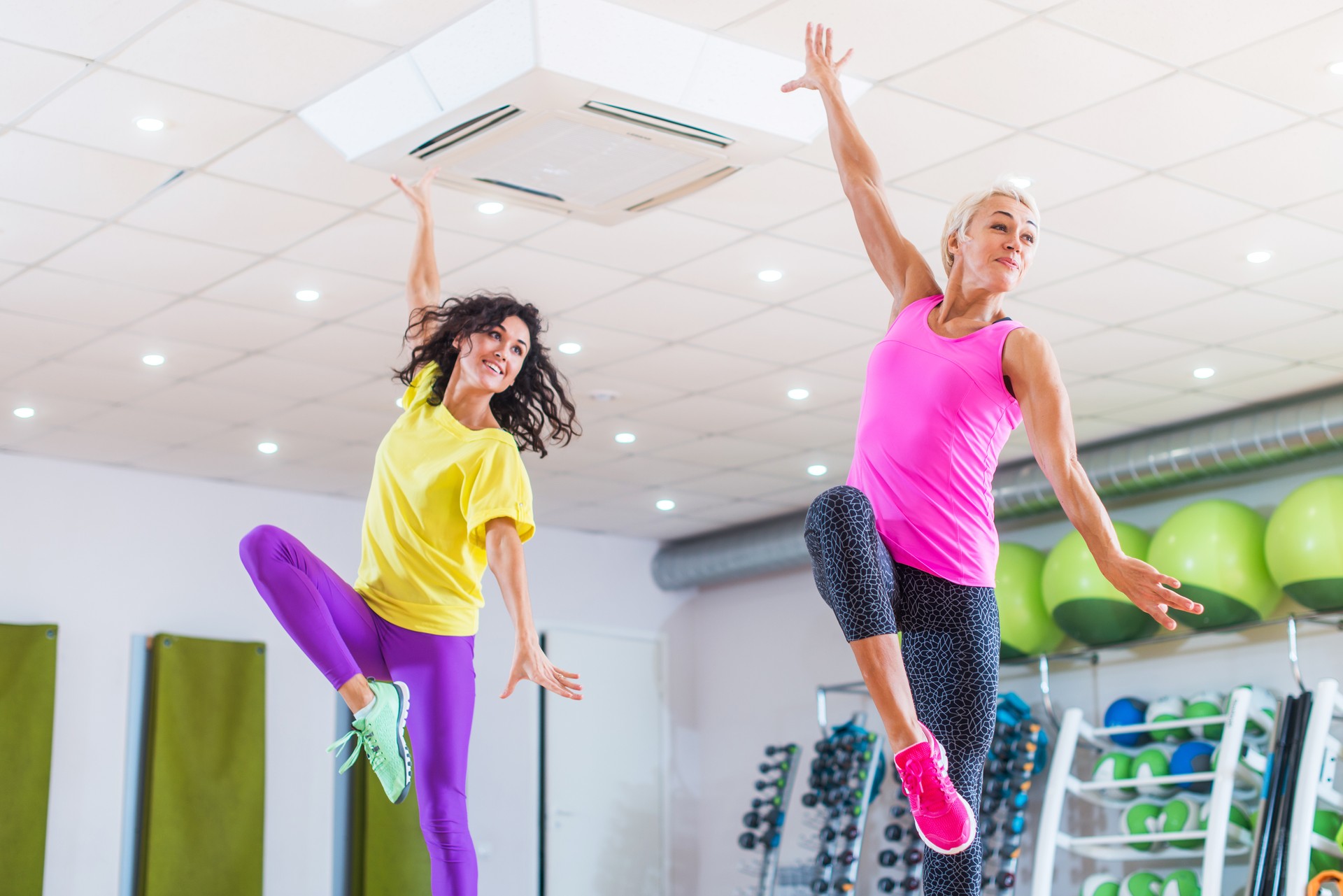 Two young sporty women exercising in fitness studio, dancing, doing cardio, working on balance and coordination.
